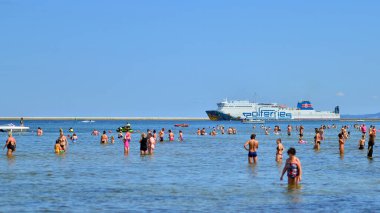 Swinoujscie, Polonya. 15 Ağustos 2023. Sahilde yıkanan insanlar. Arka planda, feribot operatörü Polferries 'in Cracovia Feribotu Polonya' daki Winoujcie 'den İsveç' teki Ystad 'a doğru yol alıyor.