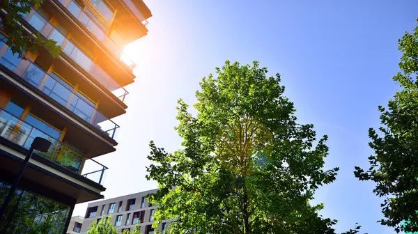 Modern apartment building and green trees. Ecological housing architecture. A modern residential building in the vicinity of trees. Ecology and green living in city, urban environment