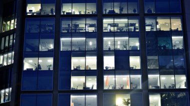 Geceleri modern bir şirket binasının cam cephesinin bir parçası. Şehirde modern cam ofis. Modern ofis binalarında geceleri büyük parlayan pencereler, pencereler ışık saçıyor.. 