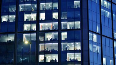Geceleri modern bir şirket binasının cam cephesinin bir parçası. Şehirde modern cam ofis. Modern ofis binalarında geceleri büyük parlayan pencereler, pencereler ışık saçıyor.. 