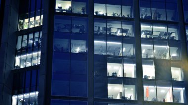 Geceleri modern bir şirket binasının cam cephesinin bir parçası. Şehirde modern cam ofis. Modern ofis binalarında geceleri büyük parlayan pencereler, pencereler ışık saçıyor.. 