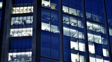 Geceleri modern bir şirket binasının cam cephesinin bir parçası. Şehirde modern cam ofis. Modern ofis binalarında geceleri büyük parlayan pencereler, pencereler ışık saçıyor.. 