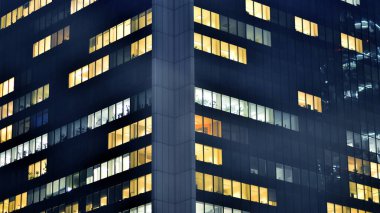 Geceleri modern bir şirket binasının cam cephesinin bir parçası. Şehirde modern cam ofis. Modern ofis binalarında geceleri büyük parlayan pencereler, pencereler ışık saçıyor.. 