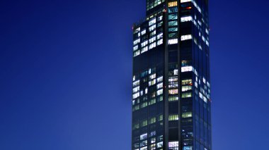 Geceleri modern bir gökdelenin cam cephesi. Şehirde modern cam ofis. Geceleri modern ofis binasında parlayan büyük pencereler. Pencere sıralarında ışık parlıyor.