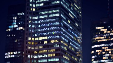 Geceleri modern gökdelenlerin cam cepheleri. Şehirde modern cam ofis. Geceleri modern ofis binalarında parlayan büyük pencereler. Pencere sıralarında ışık parlıyor.