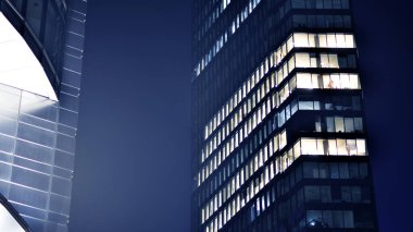 Geceleri modern gökdelenlerin cam cepheleri. Şehirde modern cam ofis. Geceleri modern ofis binalarında parlayan büyük pencereler. Pencere sıralarında ışık parlıyor.