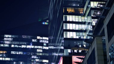 Geceleri modern gökdelenlerin cam cepheleri. Şehirde modern cam ofis. Geceleri modern ofis binalarında parlayan büyük pencereler. Pencere sıralarında ışık parlıyor.
