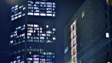 Geceleri modern gökdelenlerin cam cepheleri. Şehirde modern cam ofis. Geceleri modern ofis binalarında parlayan büyük pencereler. Pencere sıralarında ışık parlıyor.