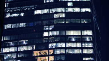 Geceleri modern bir şirket binasının cam cephesinin bir parçası. Şehirde modern cam ofis. Modern ofis binalarında geceleri büyük parlayan pencereler, pencereler ışık saçıyor.. 