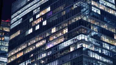 Geceleri modern gökdelenlerin cam cepheleri. Şehirde modern cam ofis. Geceleri modern ofis binalarında parlayan büyük pencereler. Pencere sıralarında ışık parlıyor.