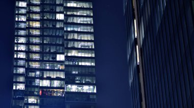 Geceleri modern gökdelenlerin cam cepheleri. Şehirde modern cam ofis. Geceleri modern ofis binalarında parlayan büyük pencereler. Pencere sıralarında ışık parlıyor.