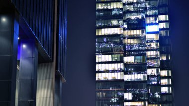 Geceleri modern gökdelenlerin cam cepheleri. Şehirde modern cam ofis. Geceleri modern ofis binalarında parlayan büyük pencereler. Pencere sıralarında ışık parlıyor.