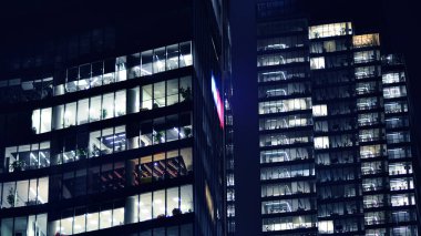 Geceleri modern gökdelenlerin cam cepheleri. Şehirde modern cam ofis. Geceleri modern ofis binalarında parlayan büyük pencereler. Pencere sıralarında ışık parlıyor.
