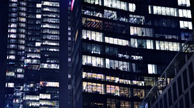 Geceleri modern gökdelenlerin cam cepheleri. Şehirde modern cam ofis. Geceleri modern ofis binalarında parlayan büyük pencereler. Pencere sıralarında ışık parlıyor.