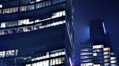 Geceleri modern gökdelenlerin cam cepheleri. Şehirde modern cam ofis. Geceleri modern ofis binalarında parlayan büyük pencereler. Pencere sıralarında ışık parlıyor.