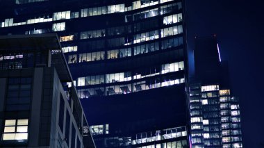 Geceleri modern gökdelenlerin cam cepheleri. Şehirde modern cam ofis. Geceleri modern ofis binalarında parlayan büyük pencereler. Pencere sıralarında ışık parlıyor.