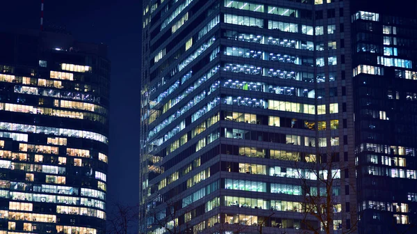 Geceleri modern gökdelenlerin cam cepheleri. Şehirde modern cam ofis. Geceleri modern ofis binalarında parlayan büyük pencereler. Pencere sıralarında ışık parlıyor.
