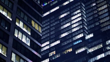 Geceleri modern gökdelenlerin cam cepheleri. Şehirde modern cam ofis. Geceleri modern ofis binalarında parlayan büyük pencereler. Pencere sıralarında ışık parlıyor.