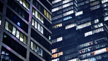 Geceleri modern gökdelenlerin cam cepheleri. Şehirde modern cam ofis. Geceleri modern ofis binalarında parlayan büyük pencereler. Pencere sıralarında ışık parlıyor.