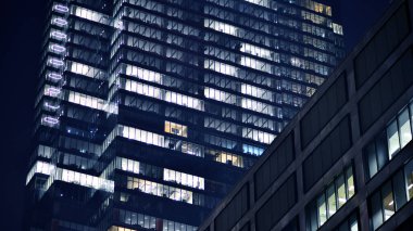 Geceleri modern gökdelenlerin cam cepheleri. Şehirde modern cam ofis. Geceleri modern ofis binalarında parlayan büyük pencereler. Pencere sıralarında ışık parlıyor.