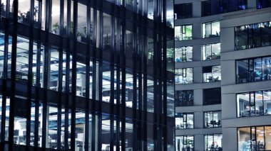 Geceleri modern gökdelenlerin cam cepheleri. Şehirde modern cam ofis. Geceleri modern ofis binalarında parlayan büyük pencereler. Pencere sıralarında ışık parlıyor.