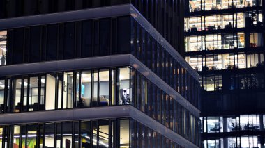 Geceleri modern gökdelenlerin cam cepheleri. Şehirde modern cam ofis. Geceleri modern ofis binalarında parlayan büyük pencereler. Pencere sıralarında ışık parlıyor.