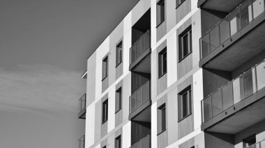Pencereleri ve balkonları olan bir binanın ön cephesi. Güneşli bir günde modern apartman binaları. Modern bir apartmanın ön cephesi. Siyah ve beyaz.