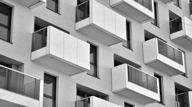 Pencereleri ve balkonları olan bir binanın ön cephesi. Güneşli bir günde modern apartman binaları. Modern bir apartmanın ön cephesi. Siyah ve beyaz.