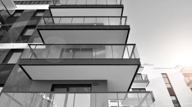 Pencereleri ve balkonları olan bir binanın ön cephesi. Güneşli bir günde modern apartman binaları. Modern bir apartmanın ön cephesi. Siyah ve beyaz.