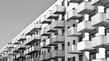 Pencereleri ve balkonları olan bir binanın ön cephesi. Güneşli bir günde modern apartman binaları. Modern bir apartmanın ön cephesi. Siyah ve beyaz.