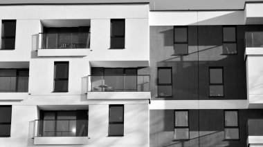 Pencereleri ve balkonları olan bir binanın ön cephesi. Güneşli bir günde modern apartman binaları. Modern bir apartmanın ön cephesi. Siyah ve beyaz.