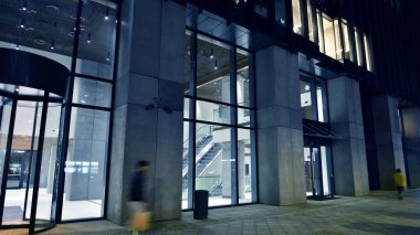 Modern ofis binasının zemin katında büyük cam pencereleri ve girişi olan gece görüşü. Sokak yansıması.