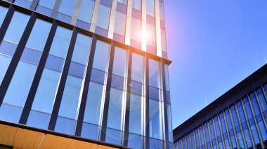 Cam cepheli modern ofis binası. Ofis binasının şeffaf cam duvarı. Binanın ön cephesinde mavi gökyüzünün yansıması.