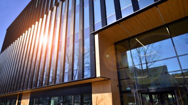 Cam cepheli modern ofis binası. Ofis binasının şeffaf cam duvarı. Binanın ön cephesinde mavi gökyüzünün yansıması.