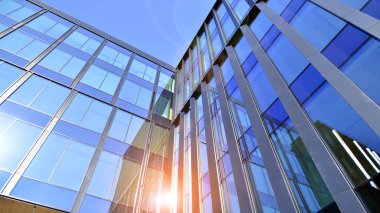 Cam cepheli modern ofis binası. Ofis binasının şeffaf cam duvarı. Binanın ön cephesinde mavi gökyüzünün yansıması.