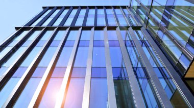 Cam cepheli modern ofis binası. Ofis binasının şeffaf cam duvarı. Binanın ön cephesinde mavi gökyüzünün yansıması.