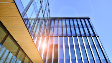 Cam cepheli modern ofis binası. Ofis binasının şeffaf cam duvarı. Binanın ön cephesinde mavi gökyüzünün yansıması.