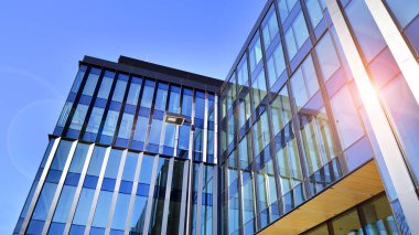 Cam cepheli modern ofis binası. Ofis binasının şeffaf cam duvarı. Binanın ön cephesinde mavi gökyüzünün yansıması.