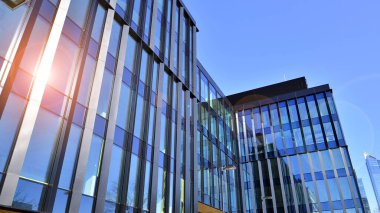 Cam cepheli modern ofis binası. Ofis binasının şeffaf cam duvarı. Binanın ön cephesinde mavi gökyüzünün yansıması.