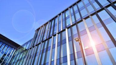 Cam cepheli modern ofis binası. Ofis binasının şeffaf cam duvarı. Binanın ön cephesinde mavi gökyüzünün yansıması.