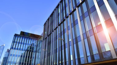 Cam cepheli modern ofis binası. Ofis binasının şeffaf cam duvarı. Binanın ön cephesinde mavi gökyüzünün yansıması.