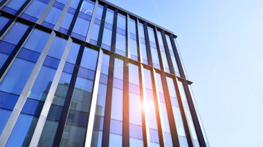 Cam cepheli modern ofis binası. Ofis binasının şeffaf cam duvarı. Binanın ön cephesinde mavi gökyüzünün yansıması.