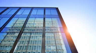 Cam cepheli modern ofis binası. Ofis binasının şeffaf cam duvarı. Binanın ön cephesinde mavi gökyüzünün yansıması.