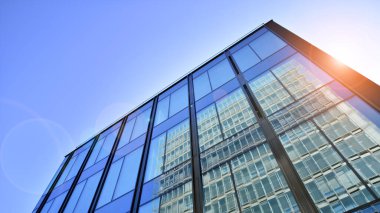 Cam cepheli modern ofis binası. Ofis binasının şeffaf cam duvarı. Binanın ön cephesinde mavi gökyüzünün yansıması.