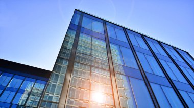 Cam cepheli modern ofis binası. Ofis binasının şeffaf cam duvarı. Binanın ön cephesinde mavi gökyüzünün yansıması.