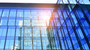 Cam cepheli modern ofis binası. Ofis binasının şeffaf cam duvarı. Binanın ön cephesinde mavi gökyüzünün yansıması.