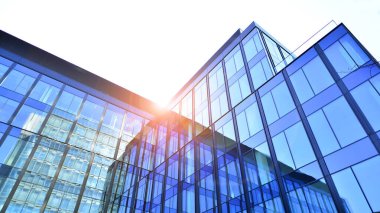 Cam cepheli modern ofis binası. Ofis binasının şeffaf cam duvarı. Binanın ön cephesinde mavi gökyüzünün yansıması.