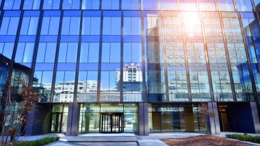 Cam cepheli modern ofis binası. Ofis binasının şeffaf cam duvarı. Binanın ön cephesinde mavi gökyüzünün yansıması.