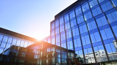 Cam cepheli modern ofis binası. Ofis binasının şeffaf cam duvarı. Binanın ön cephesinde mavi gökyüzünün yansıması.