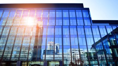 Cam cepheli modern ofis binası. Ofis binasının şeffaf cam duvarı. Binanın ön cephesinde mavi gökyüzünün yansıması.